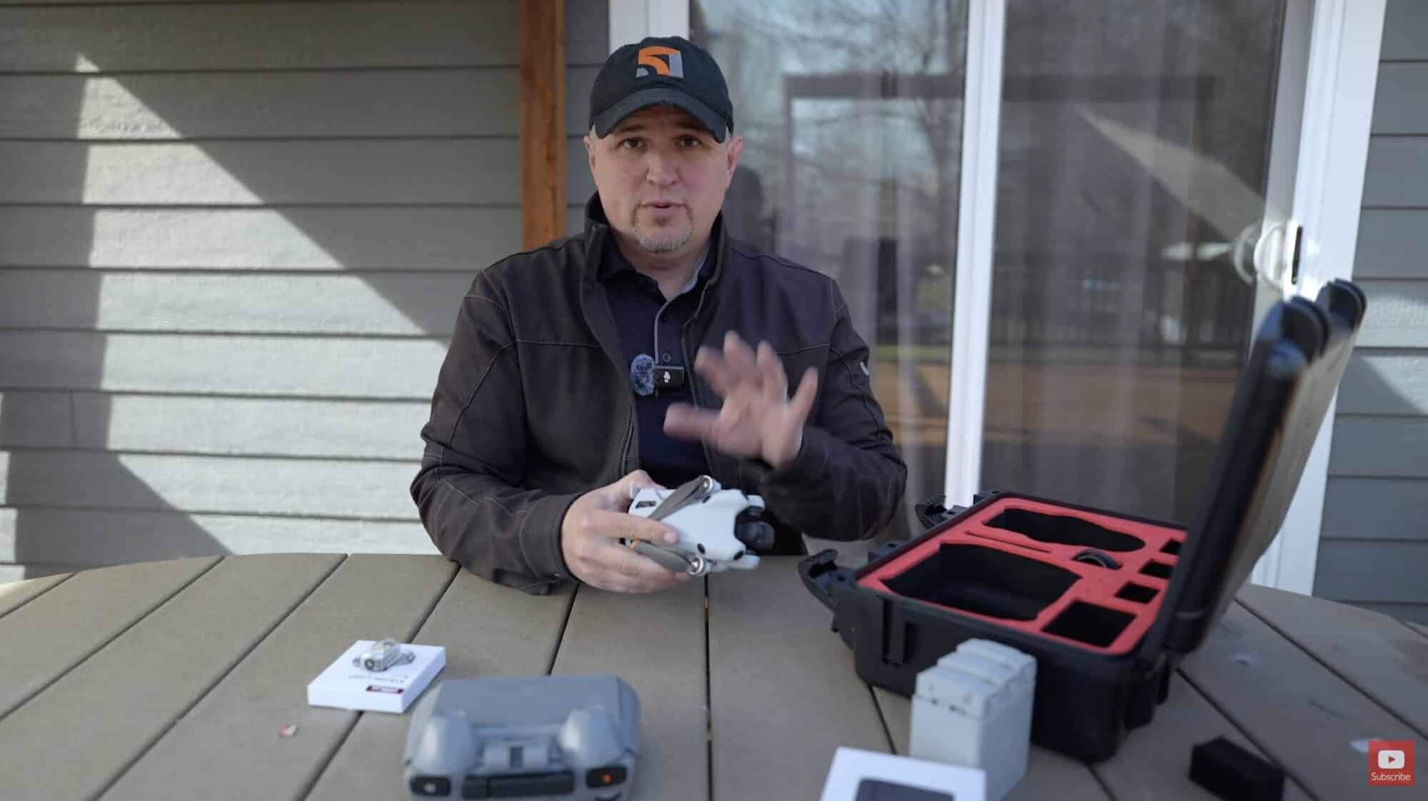 Reviewer at an outdoor table holding a DJI Mini 4 Pro beside an open case.