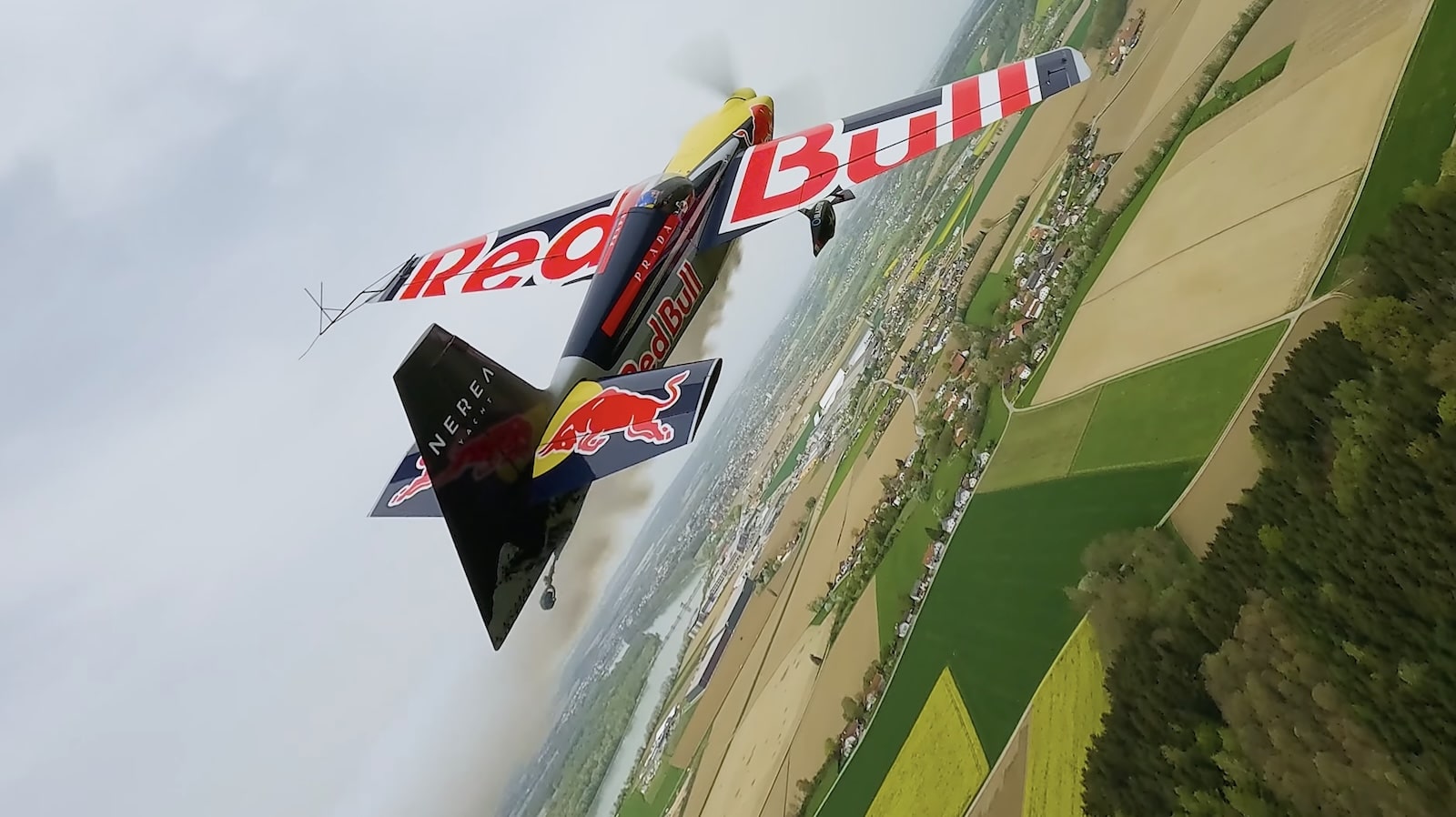 A Red Bull racing plane banks low over patchwork farmland during the run.
