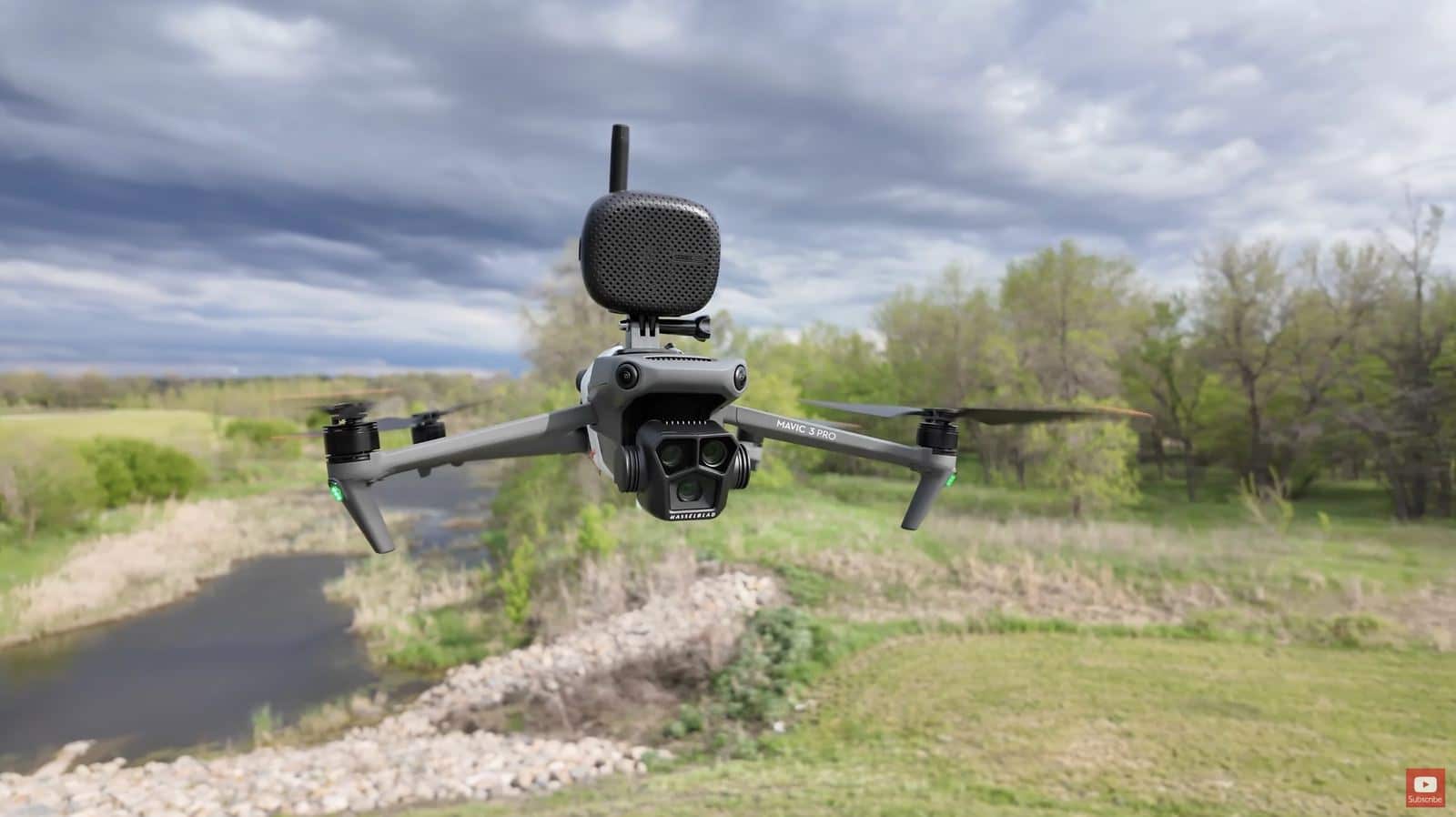 DJI Mavic 3 Pro hovering over a creek, speaker clamped above its triple camera.