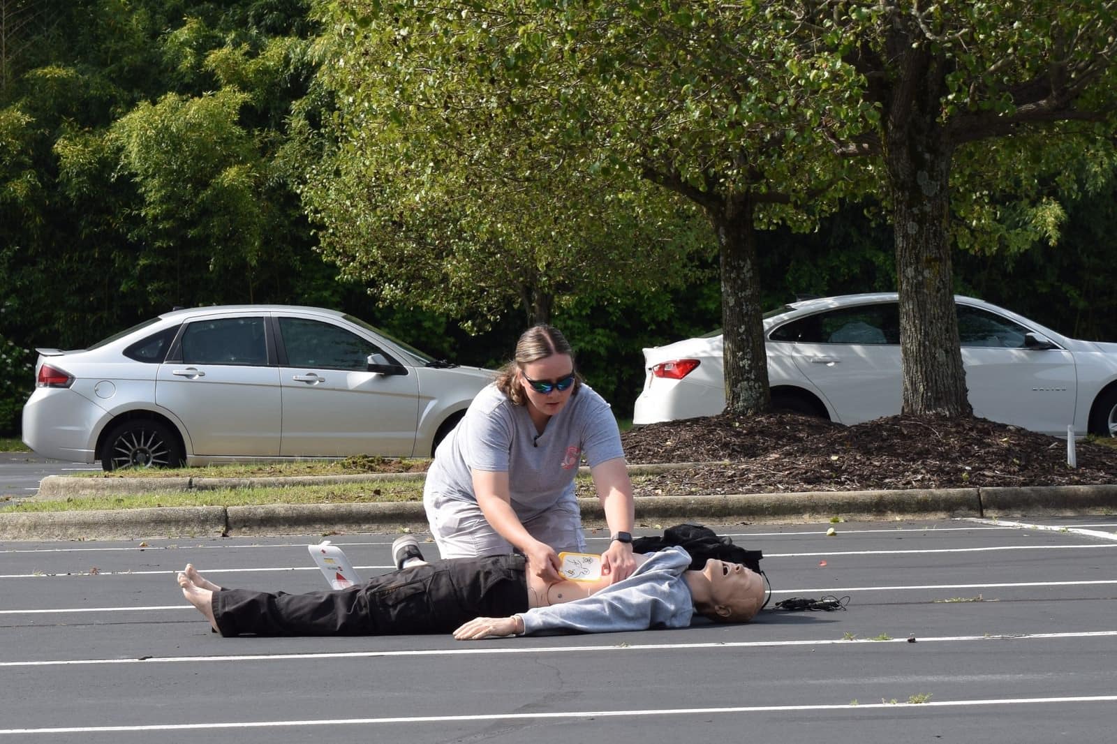 Responder performing chest compressions on a training manikin in a parking lot.