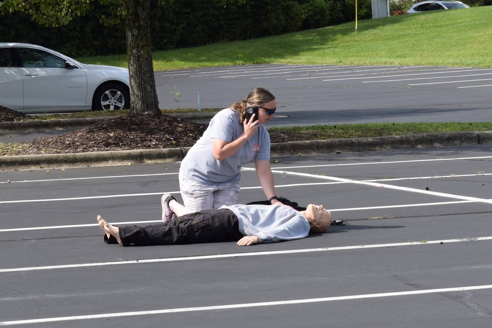 Responder kneeling beside the manikin while calling for help on a cell phone.