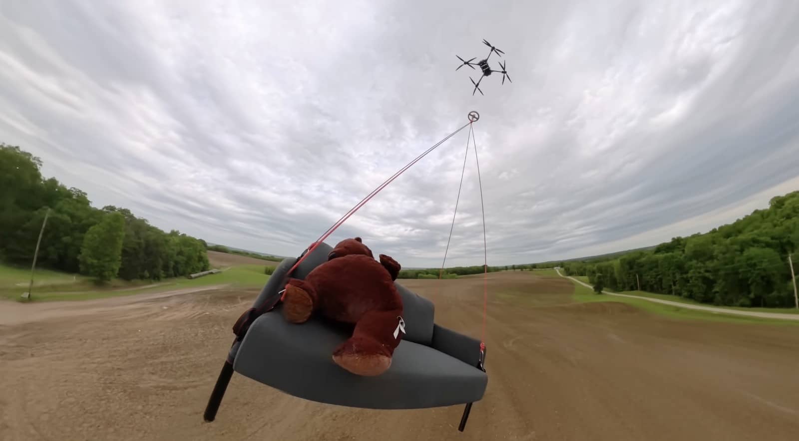 DJI FlyCart 30 winching a couch and teddy bear over a dirt track.