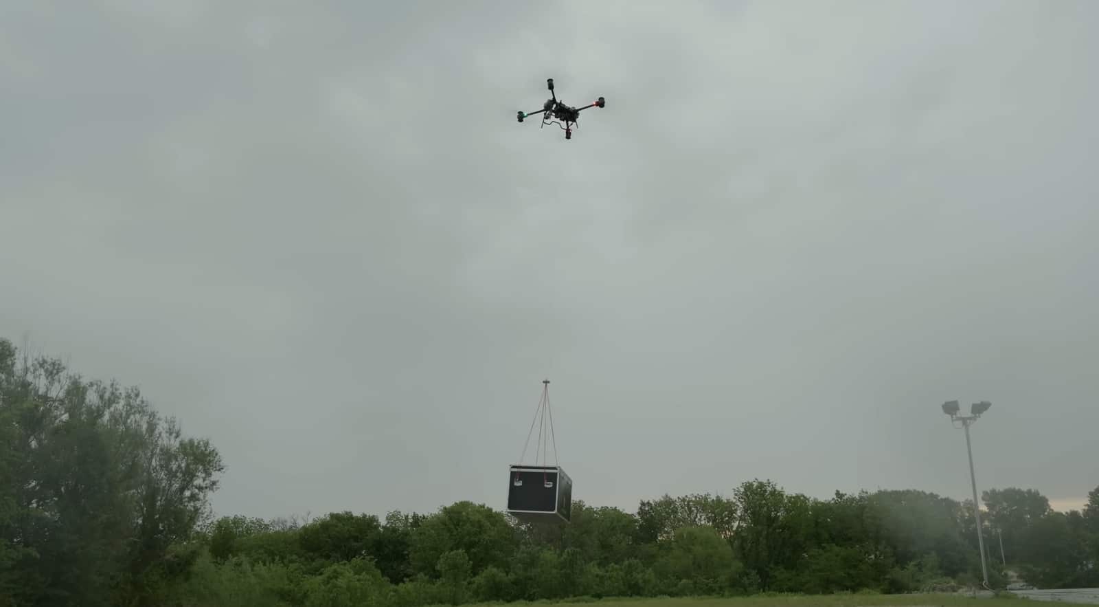 FlyCart 30 hovering under grey cloud with a black case slung beneath it.