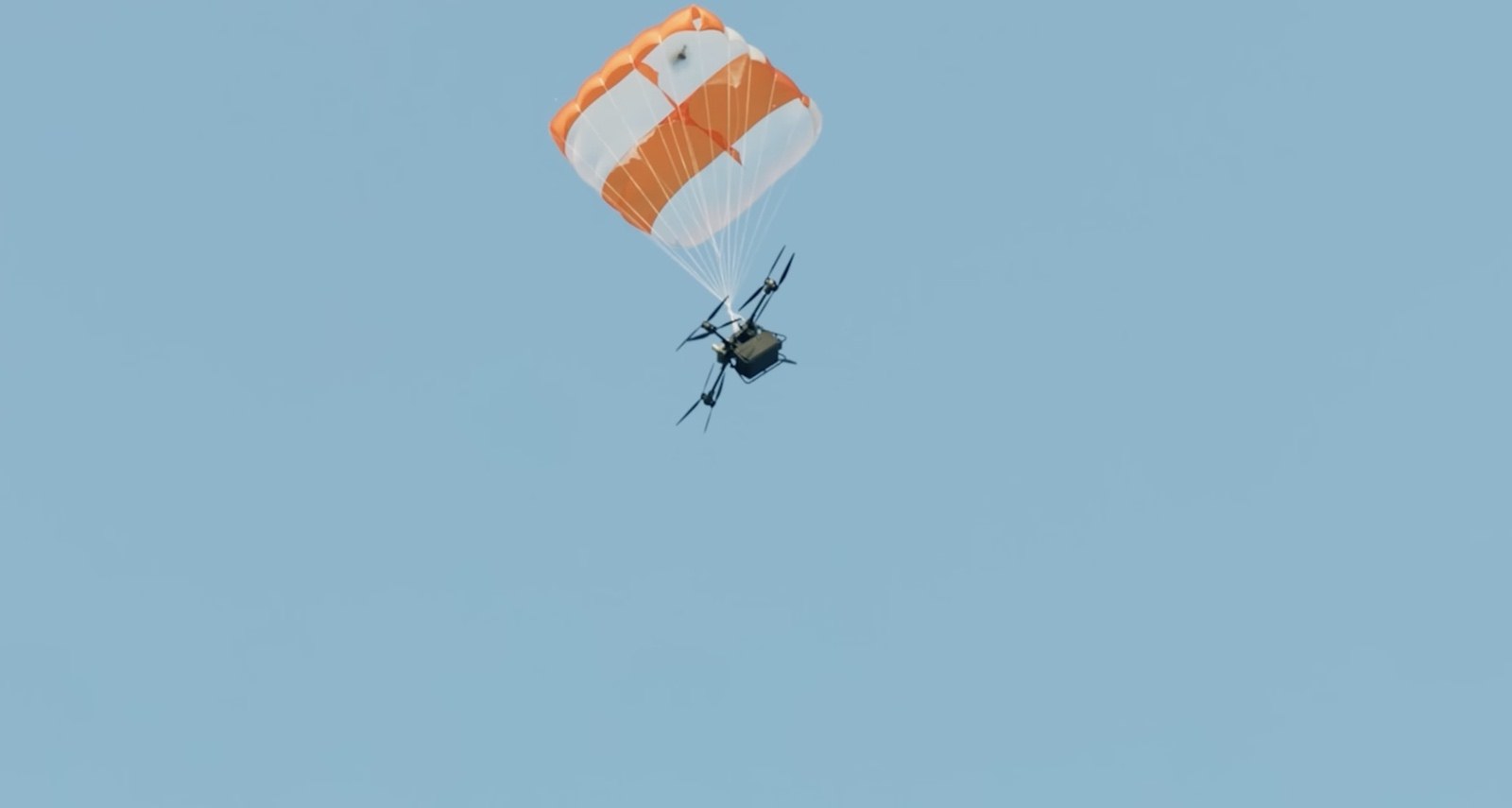 FlyCart 30 descending under a fully open orange and white recovery parachute.