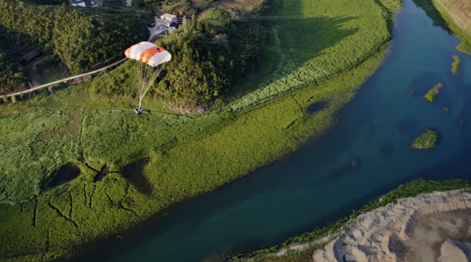 Parachute-borne FlyCart 30 drifting toward a green riverbank seen from above.