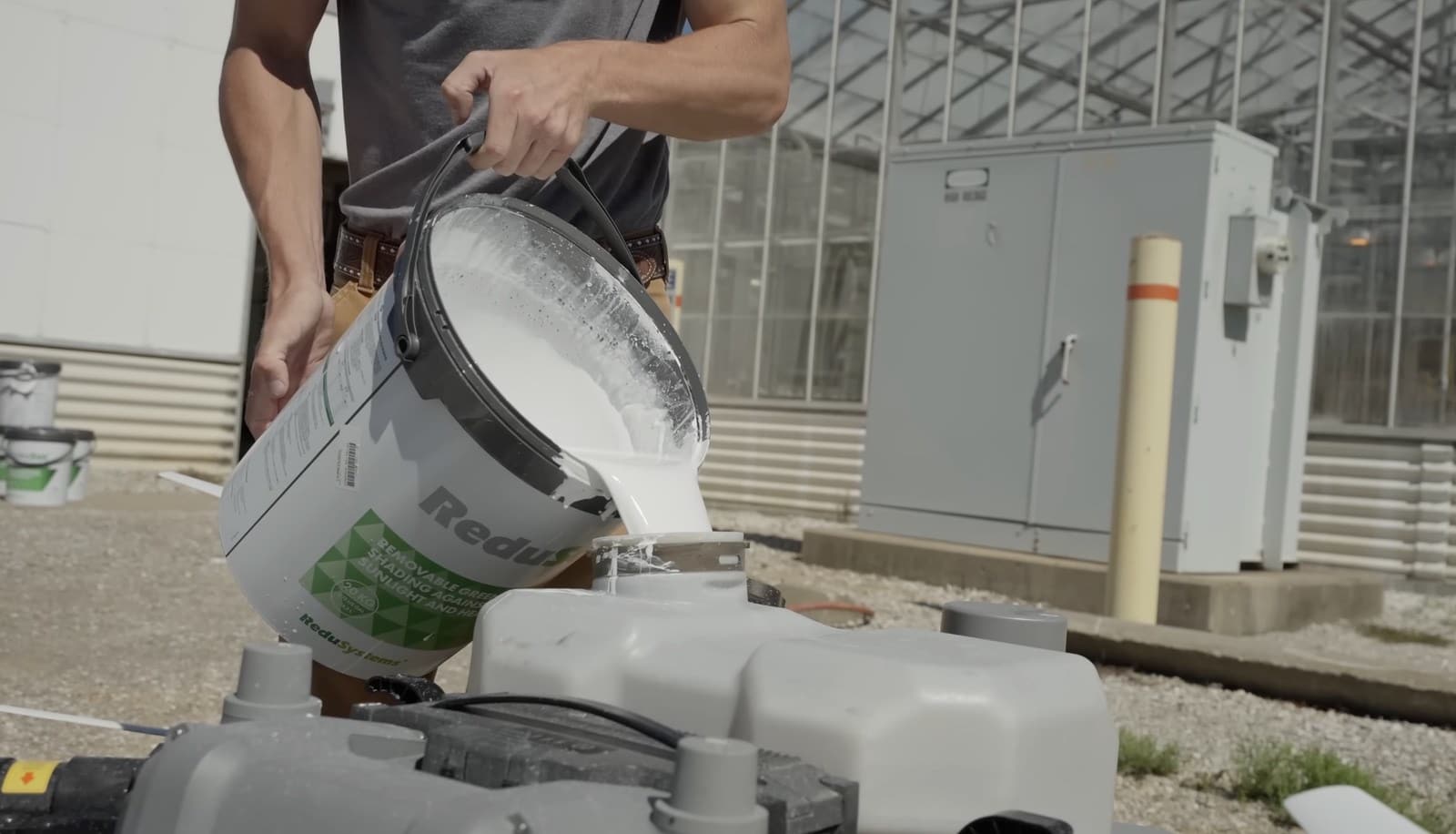 Worker pouring white coating from a bucket into an agricultural drone tank.