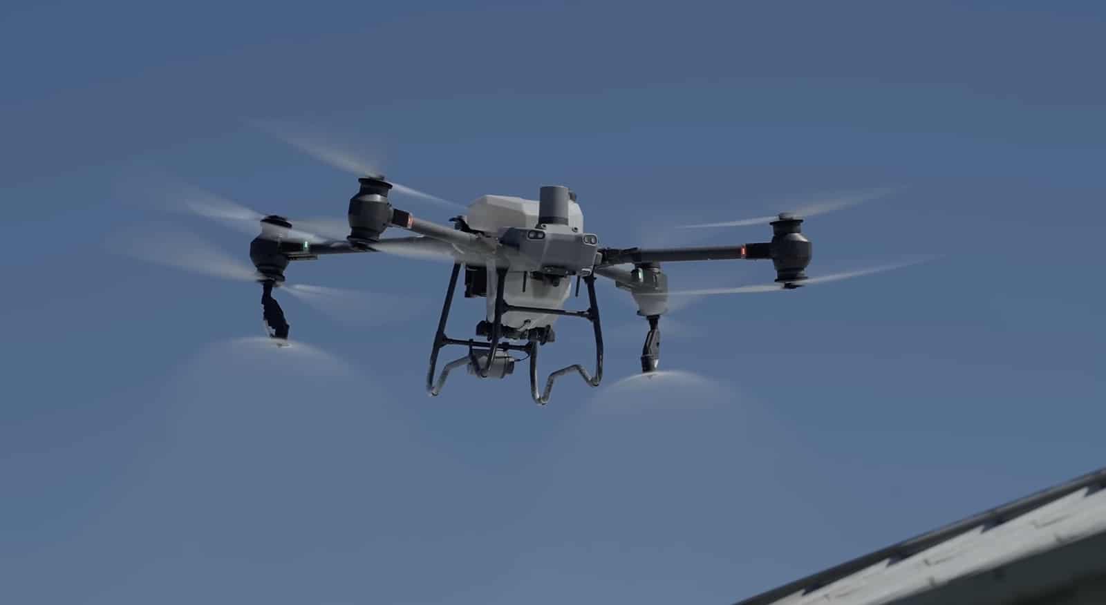 Spray drone releasing mist from its nozzles against a clear blue sky.