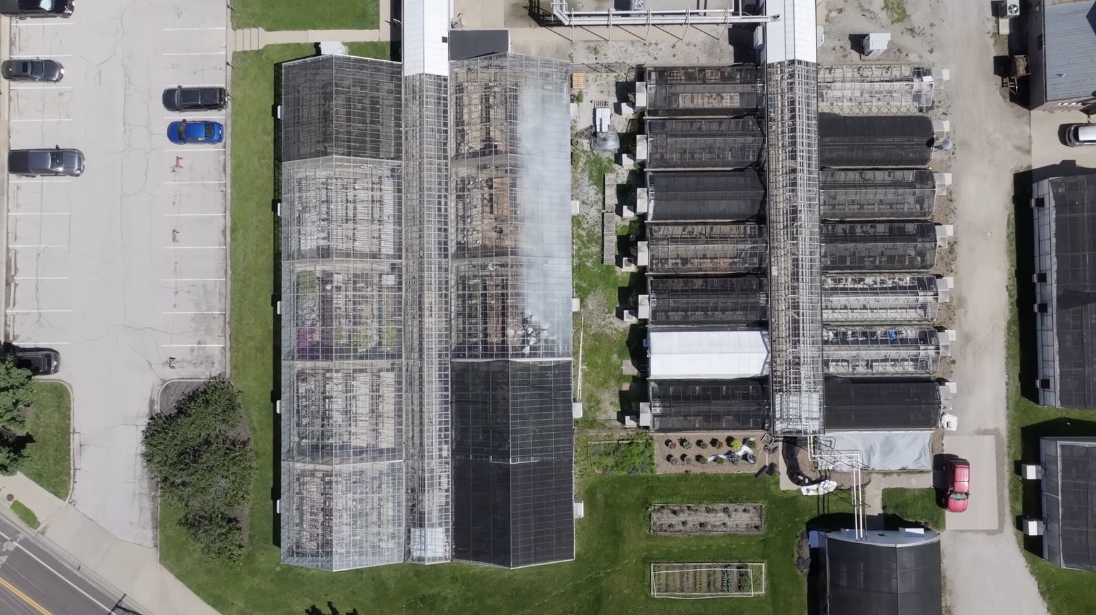 Overhead view of a greenhouse complex with parking lot and service buildings.