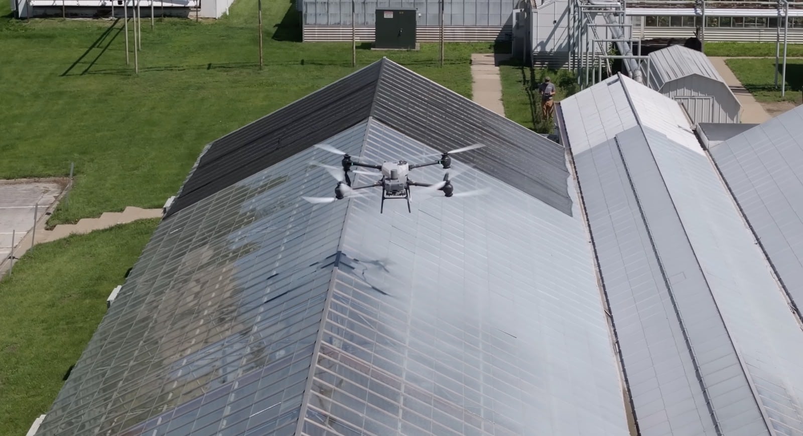 Spray drone hovering just above the ridge of a glasshouse roof.