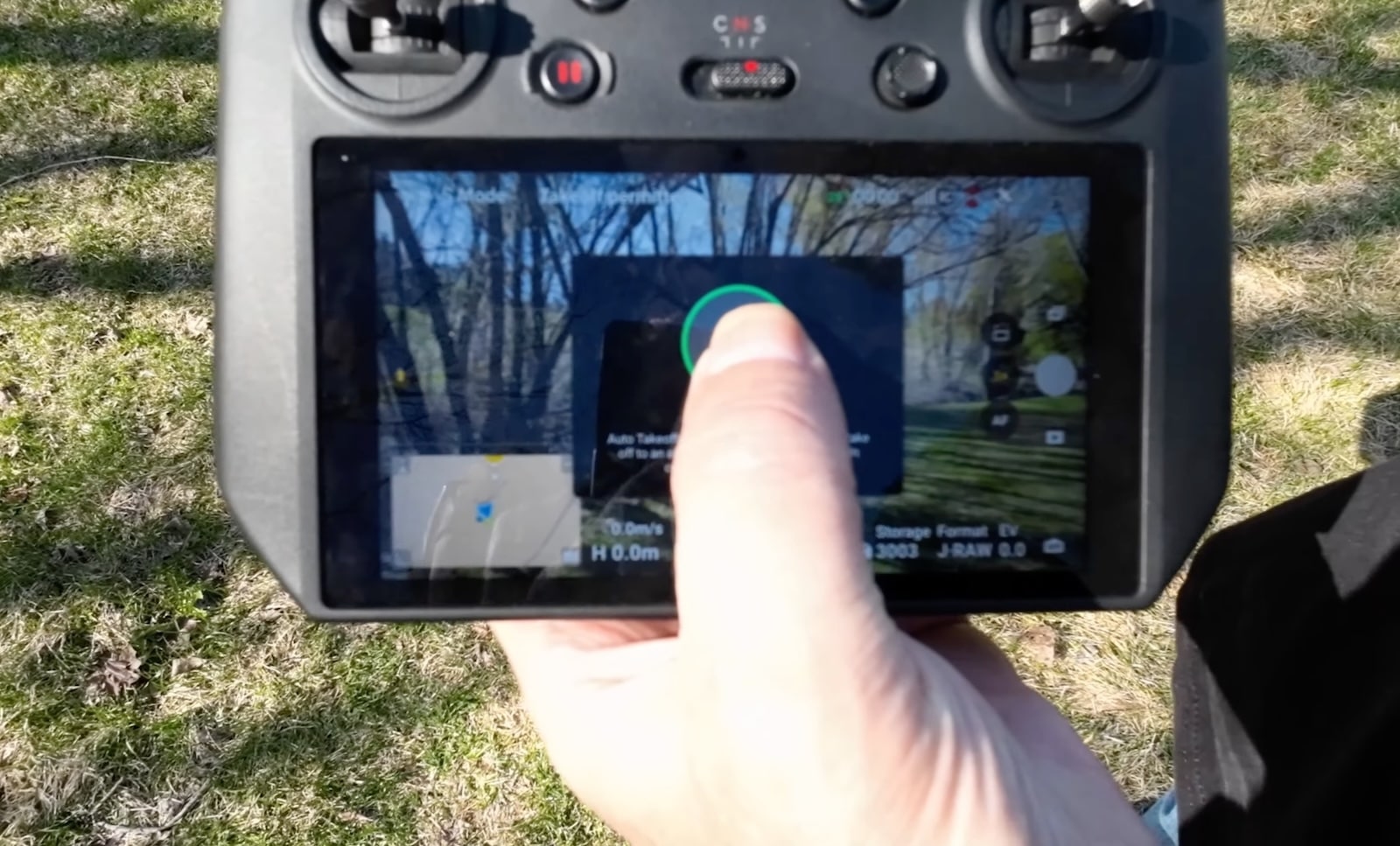 Thumb pressing the auto takeoff control on a DJI controller screen outdoors.