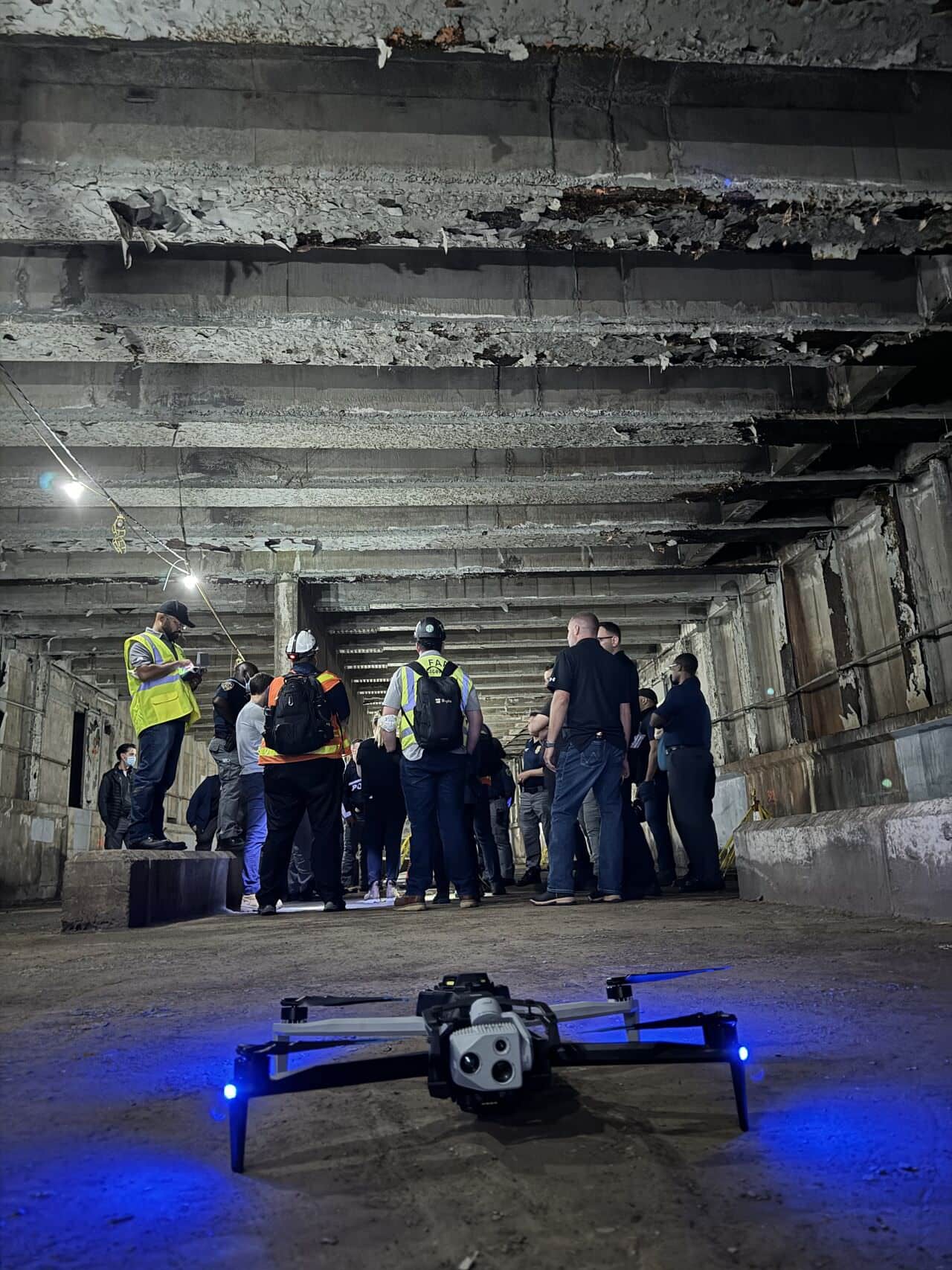 A drone glows blue on the subway tunnel floor as onlookers watch.
