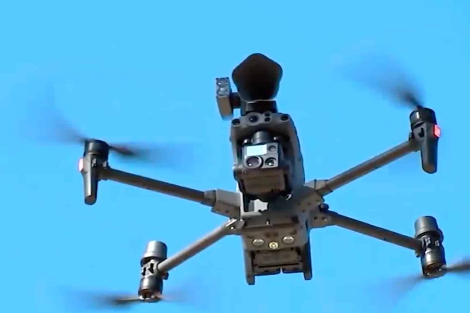 A DJI Matrice 30 with a loudspeaker mounted on top flies against blue sky.