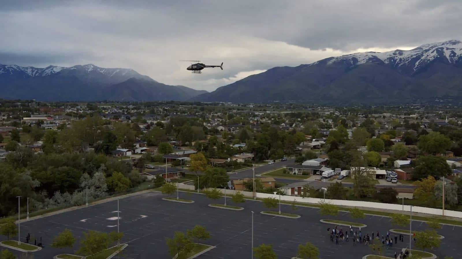 Helicopter climbing above a parking lot vertiport with snowy Utah mountains behind.