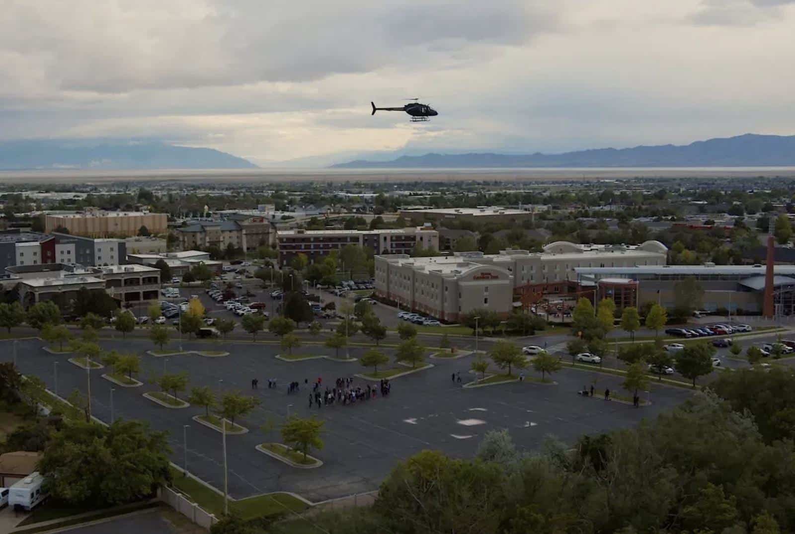 Black helicopter lifting away from a parking lot vertiport as spectators watch.