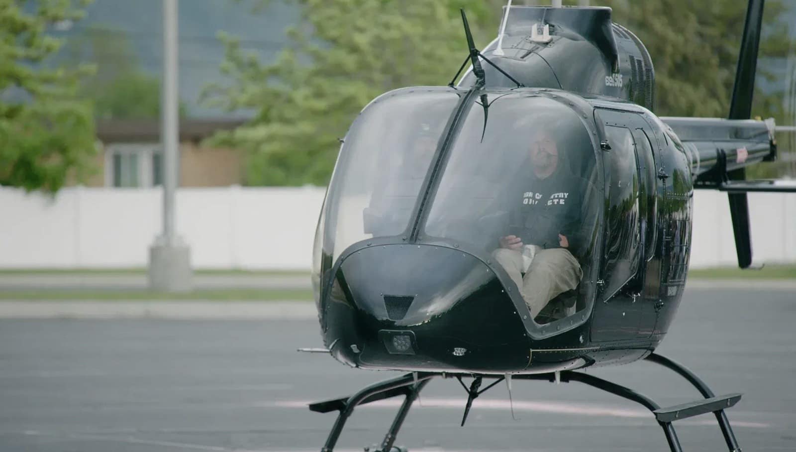 Pilot seated in a black helicopter idling on the paved vertiport.