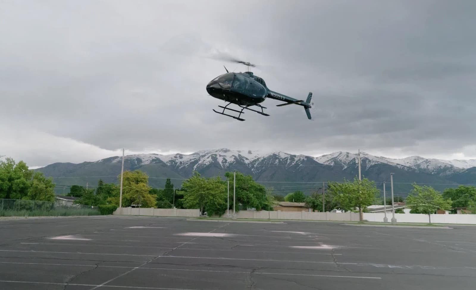 Helicopter hovering above an empty lot with the snowy Wasatch Range behind.