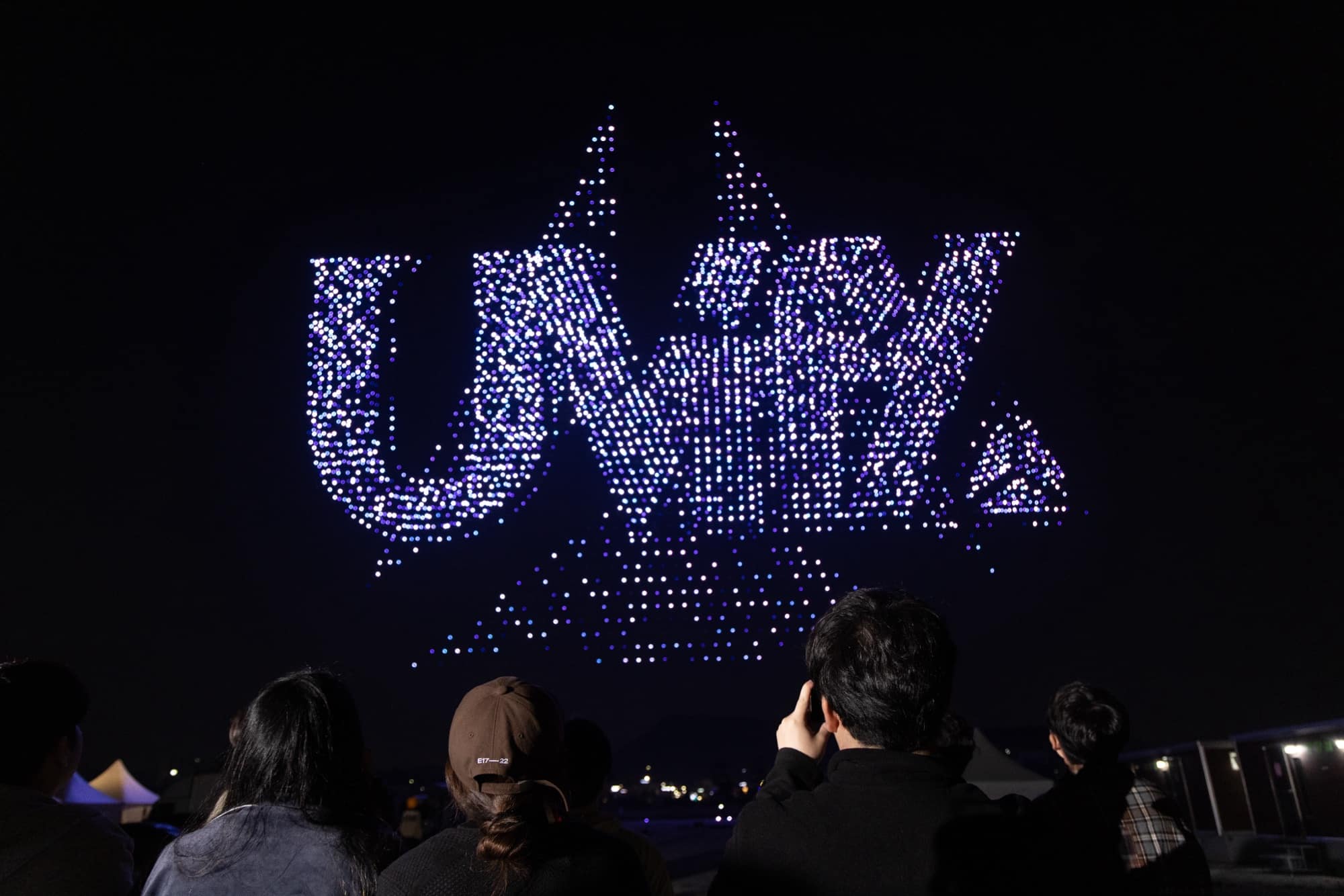 Drone swarm spelling the UVify logo in the night sky above spectators.