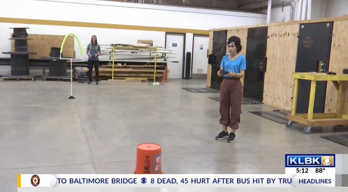 News frame of students flying a small drone through hoops in a college workshop.