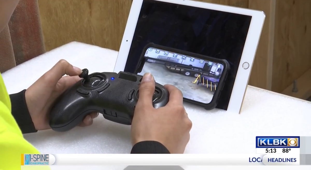News frame of hands on a controller with a tablet showing the drone feed.