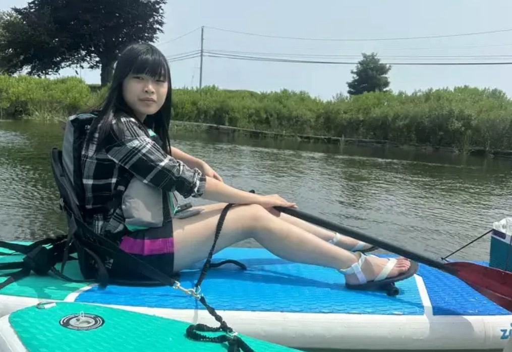 Young researcher in a life vest sits on a paddleboard in a marsh channel.