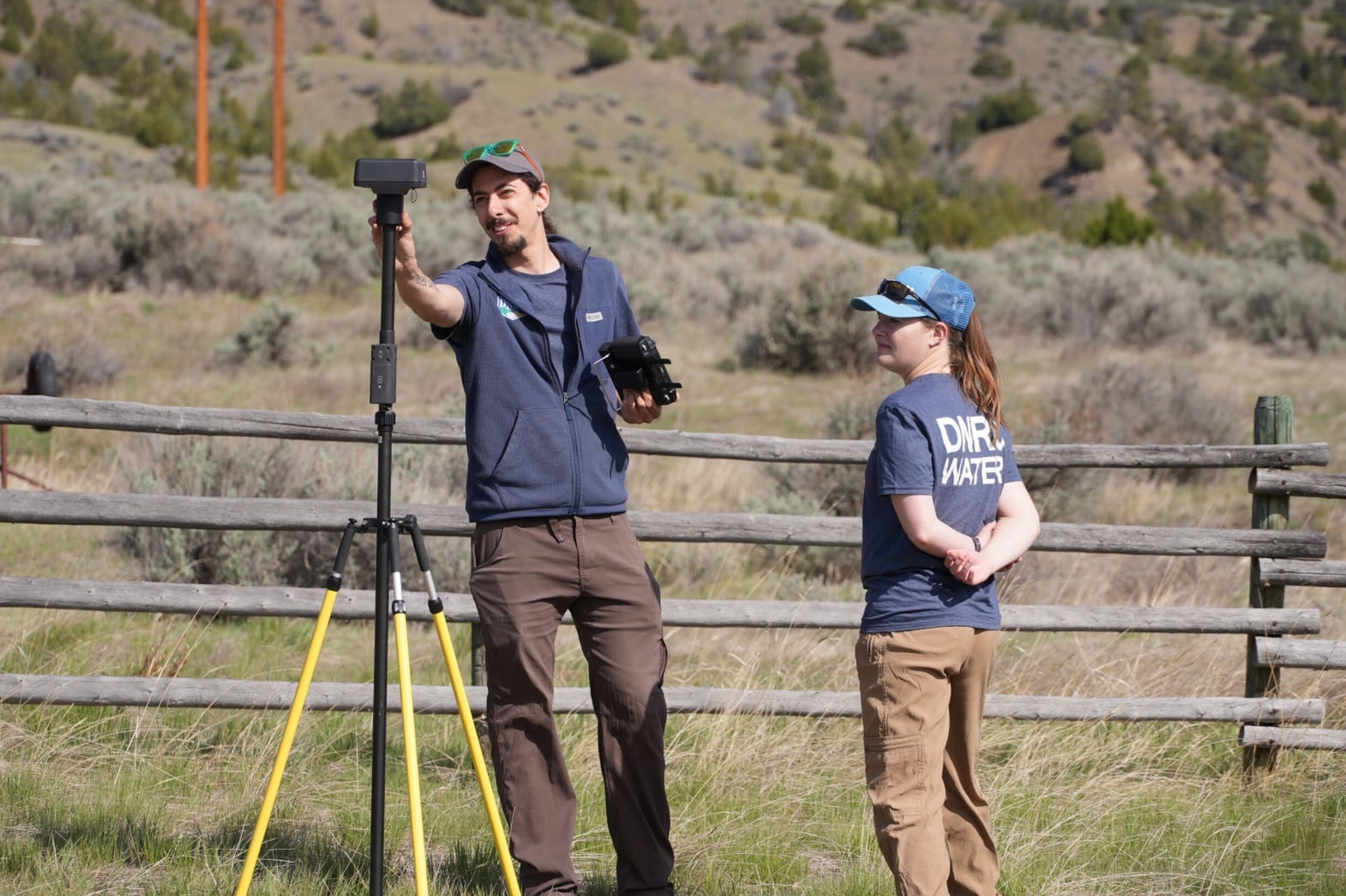 Two DNRC staff with a survey antenna on a tripod in sagebrush rangeland.