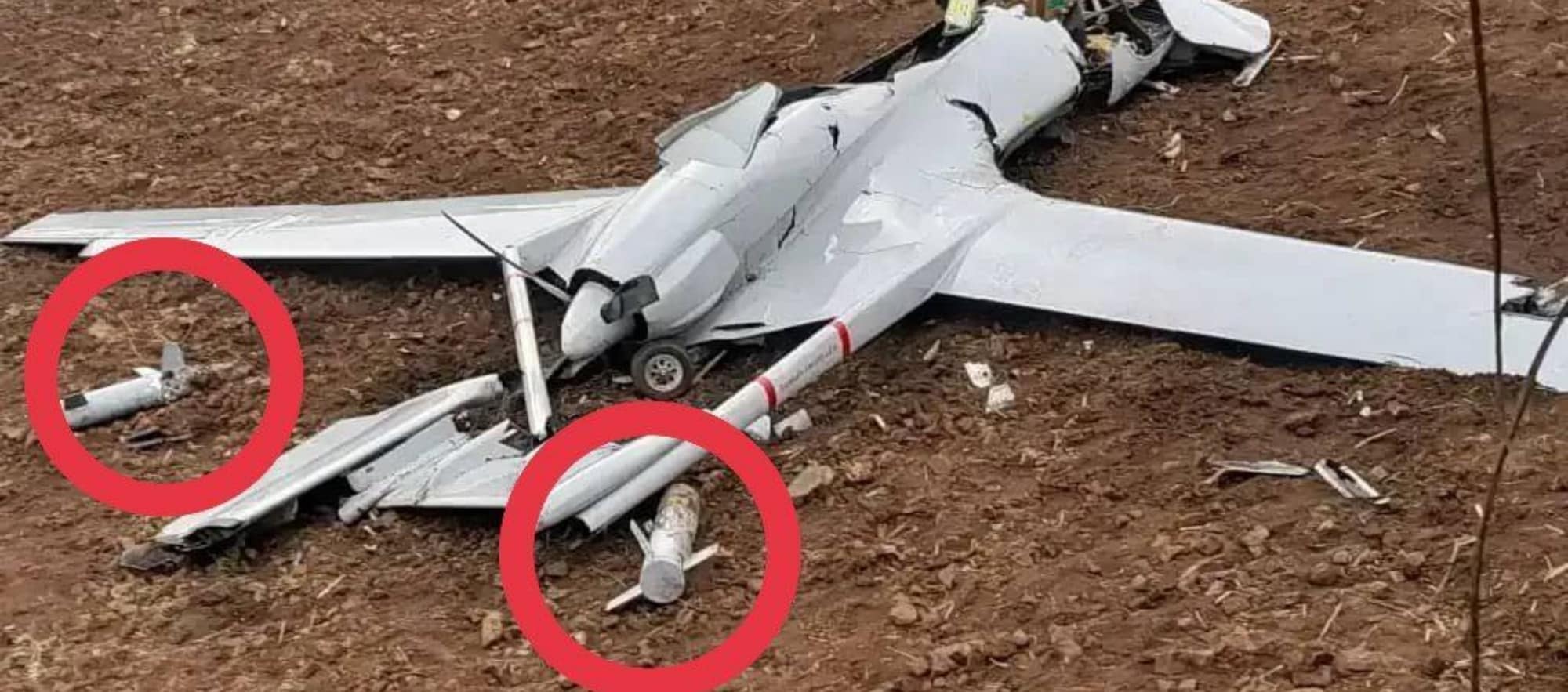Wreckage of a downed Bayraktar TB2 in red soil with two munitions circled.
