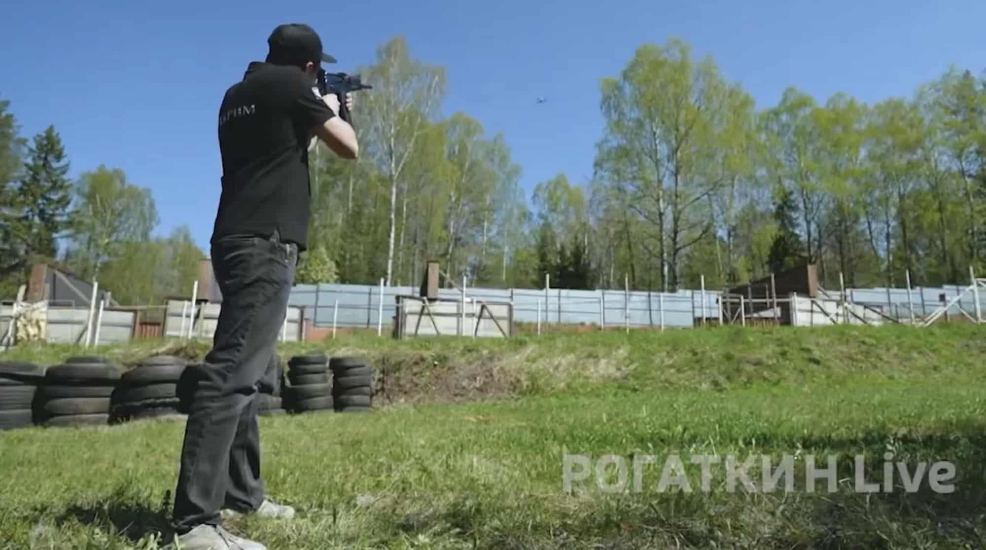Man shouldering a shotgun aimed skyward on a grass range lined with tires.