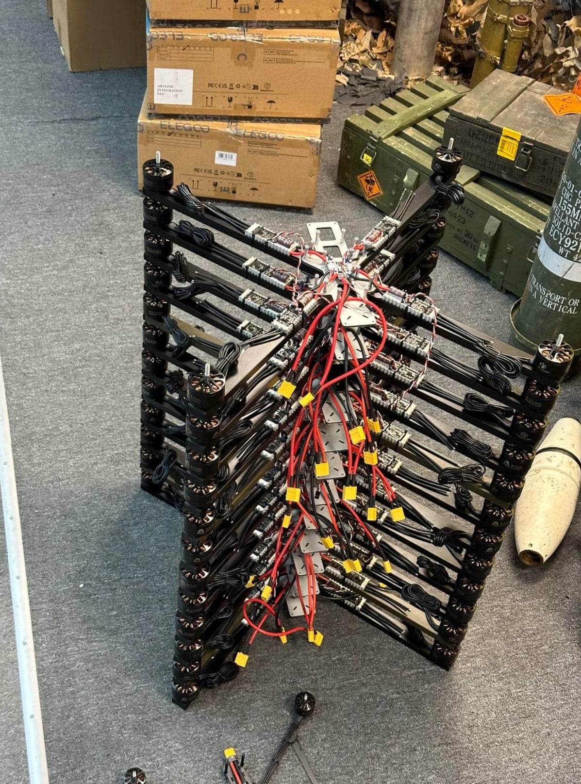 Stacked FPV drone frames with wiring bundles beside ammunition crates in a workshop.