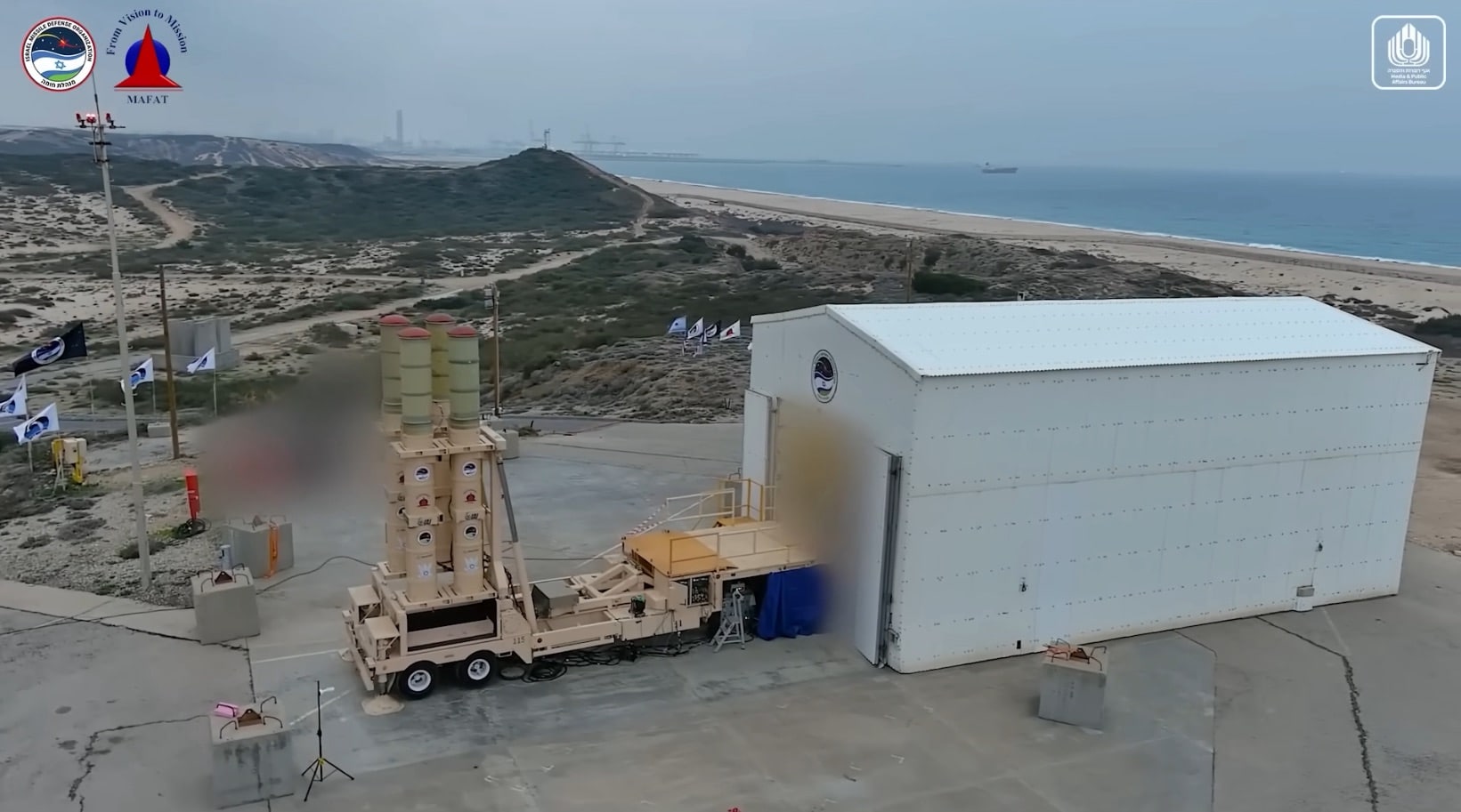 Arrow 3 launcher raised on a coastal test pad flanked by Israeli flags.