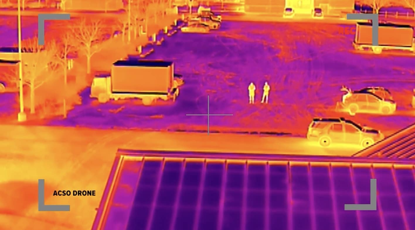 Thermal drone footage picking out two people standing in a parking lot.