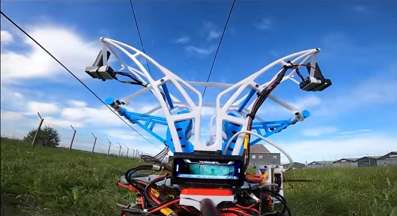 The drone's white gripper arms reaching up toward an overhead power line.