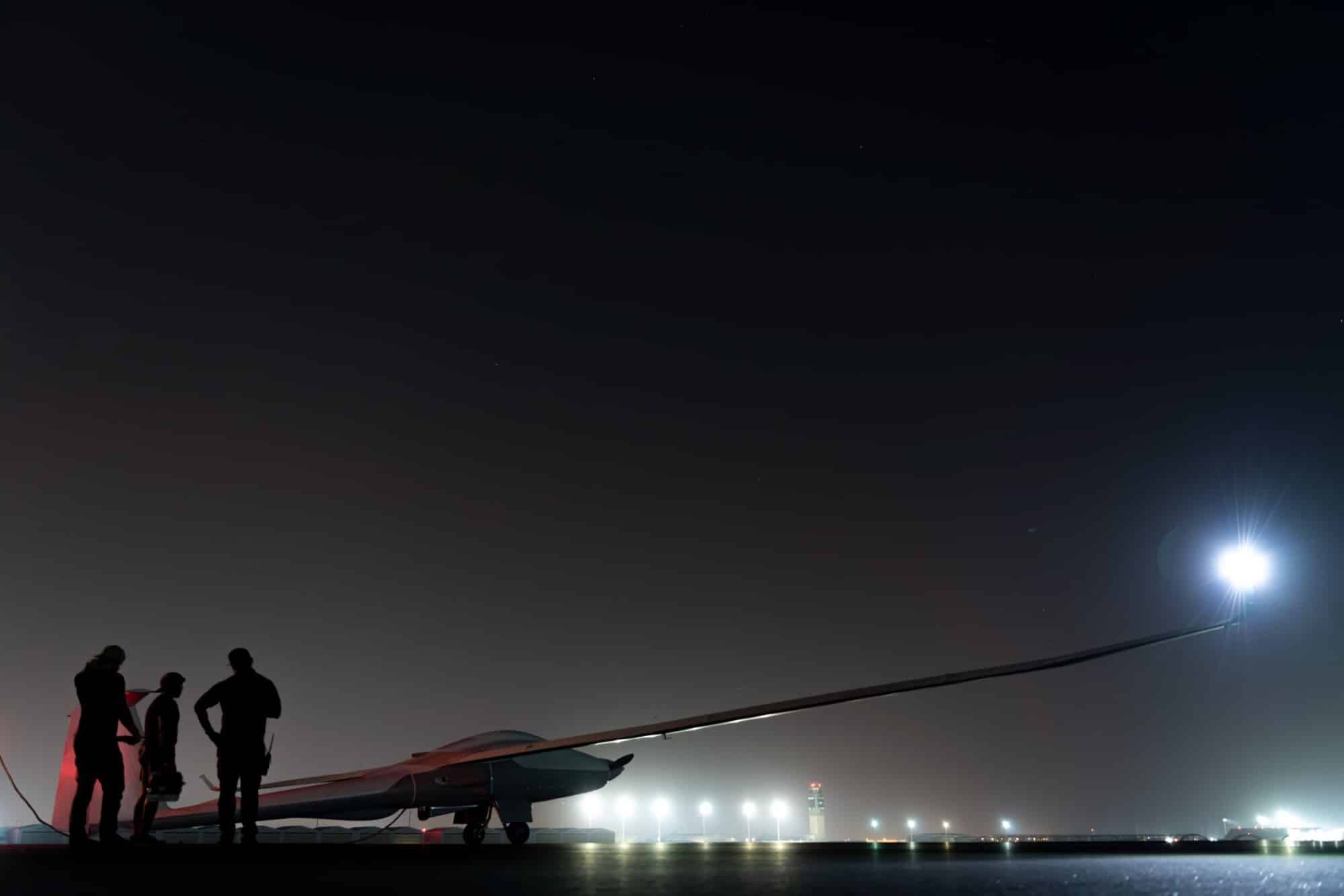 Crew silhouetted beside the sailplane-like drone on the night flight line.