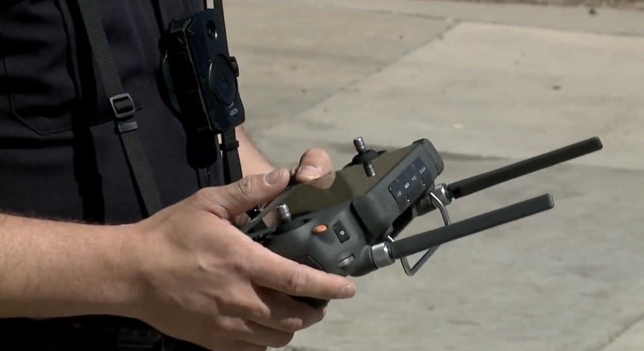 An officer's hands work the drone controller with its antennas extended.