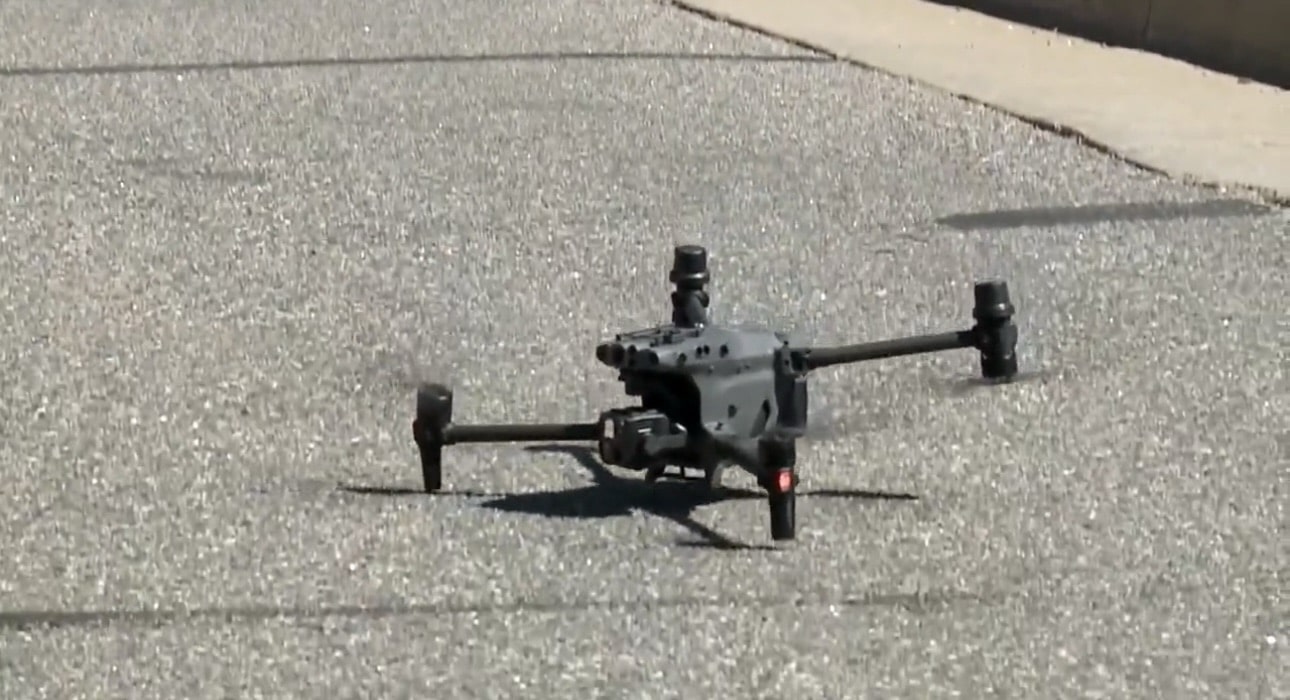 A folding quadcopter hovers a few feet above a parking lot surface.