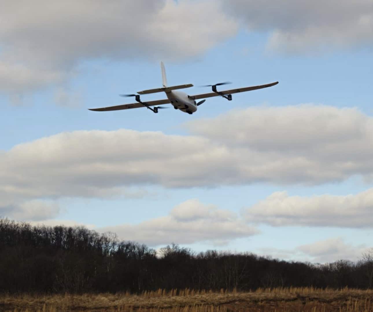 Twin-engine fixed-wing drone flying low over a bare winter field.