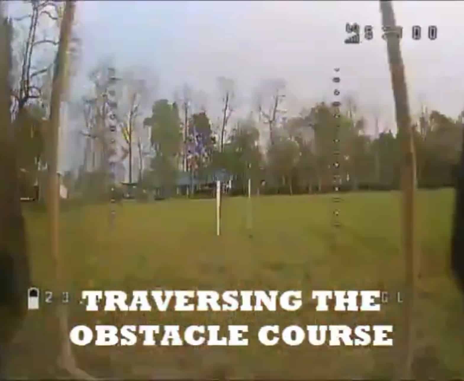 Grainy FPV drone footage captioned traversing the obstacle course over an open field.