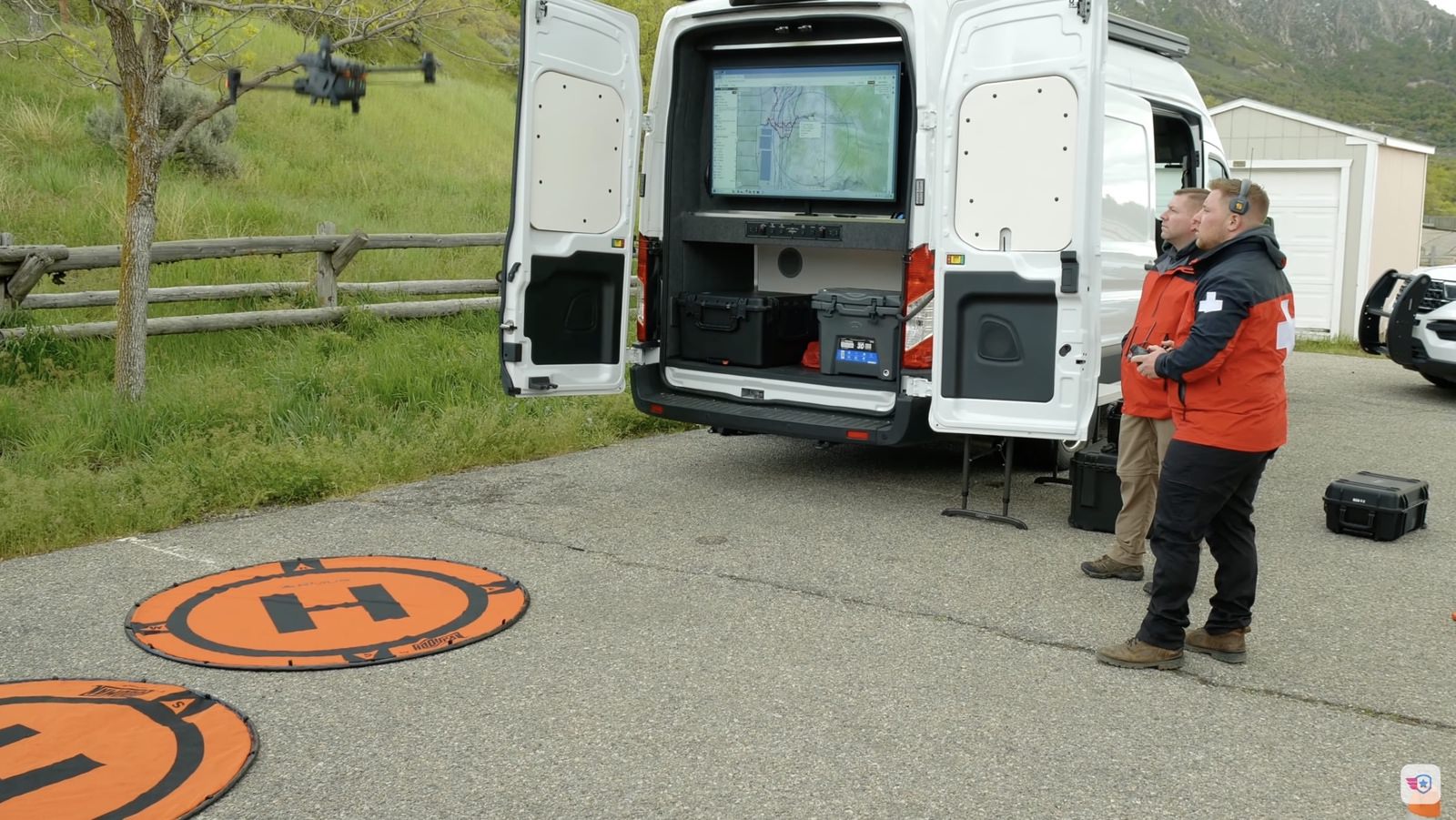 White command van with an orange landing pad and two team members on a canyon road.