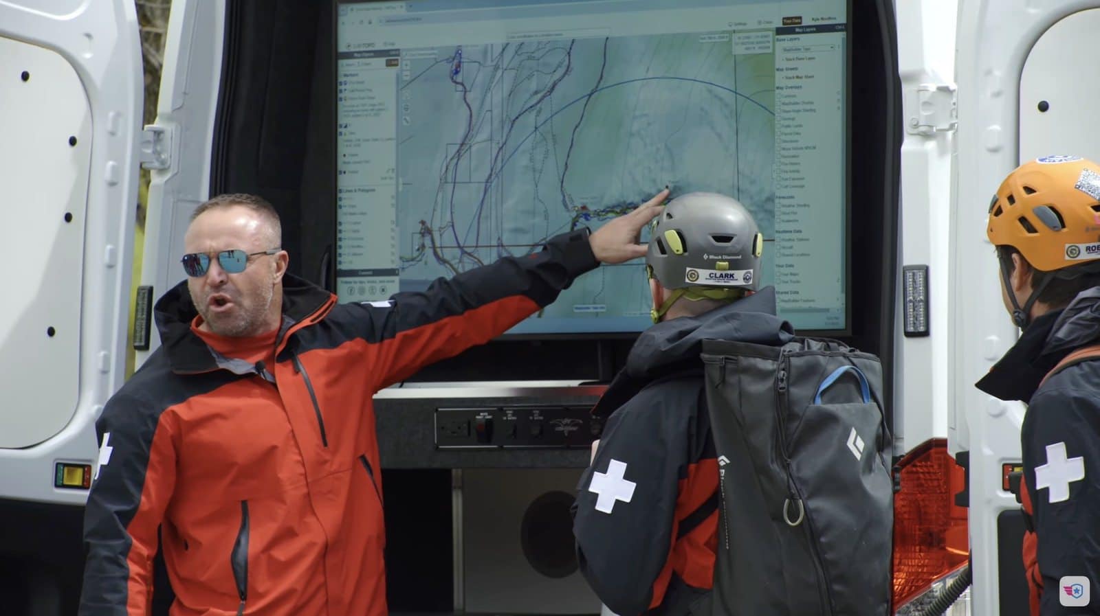 Commander talking through the search plan with an arm raised toward the map screen.