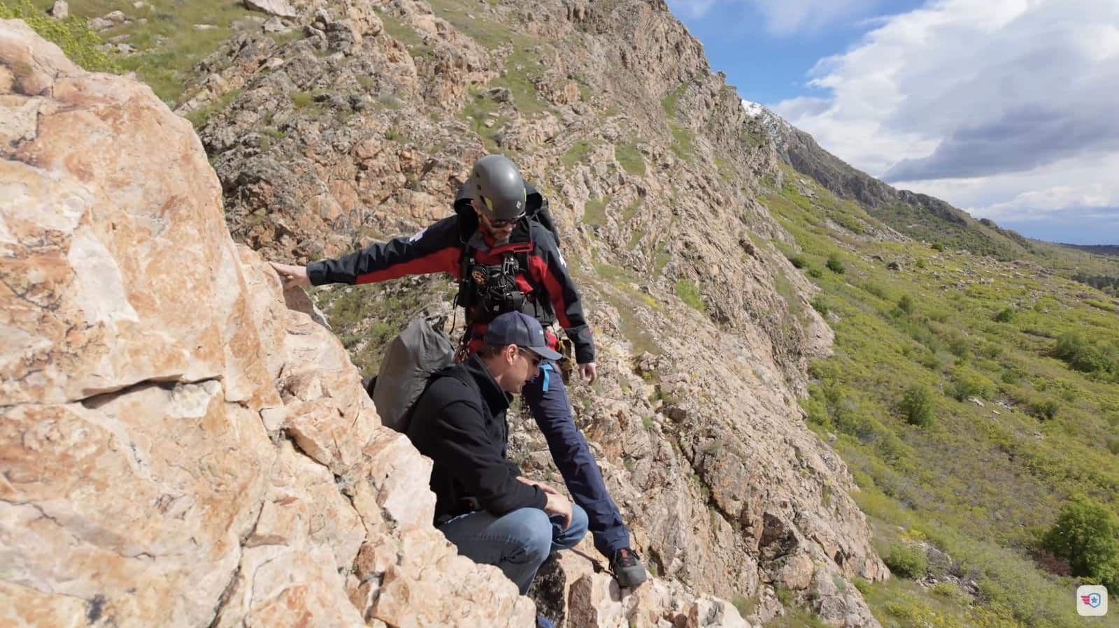 Rescuer steadying the hiker crouched below him on a rock outcrop.