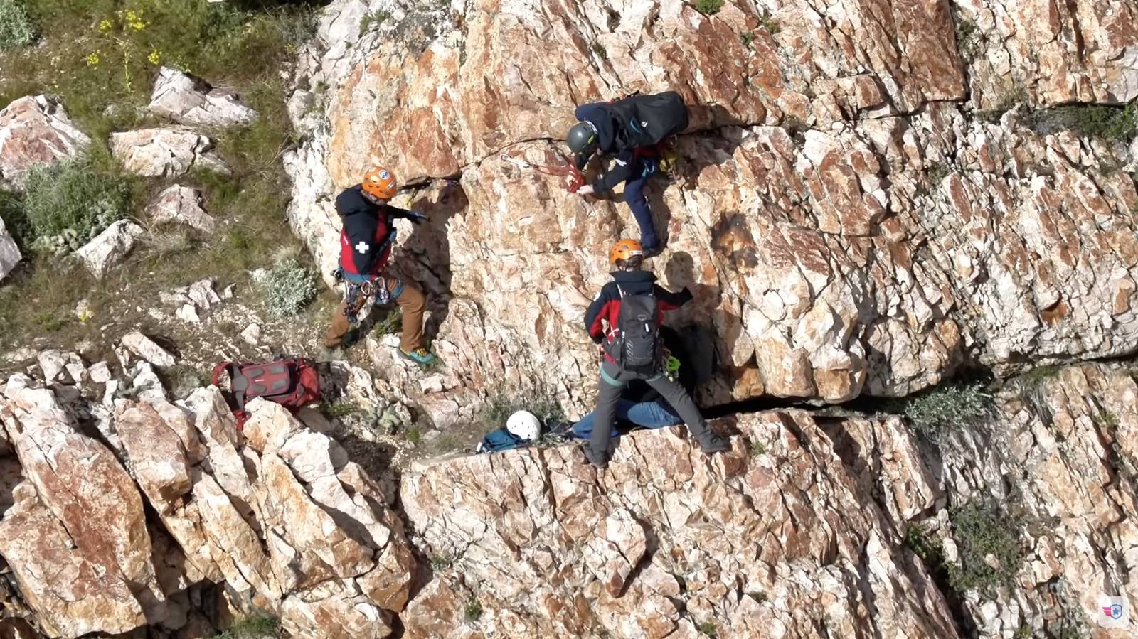 Two rescuers working their way down a white rock face above a green valley.