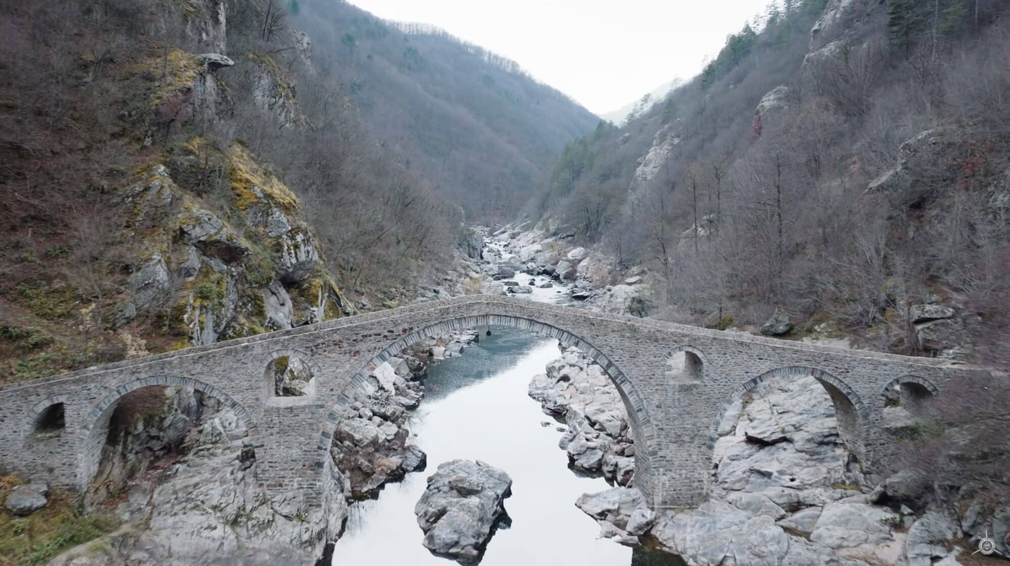 Aerial of an old stone arch bridge crossing a river in a rocky gorge.