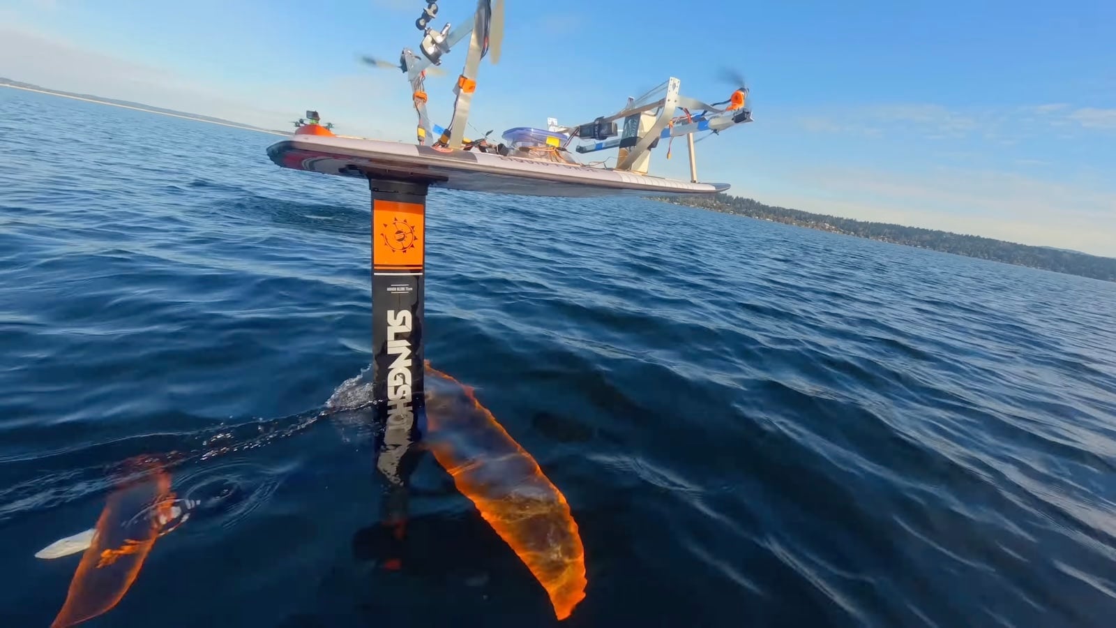 Close view of the board riding its foil mast with the orange front wing submerged.
