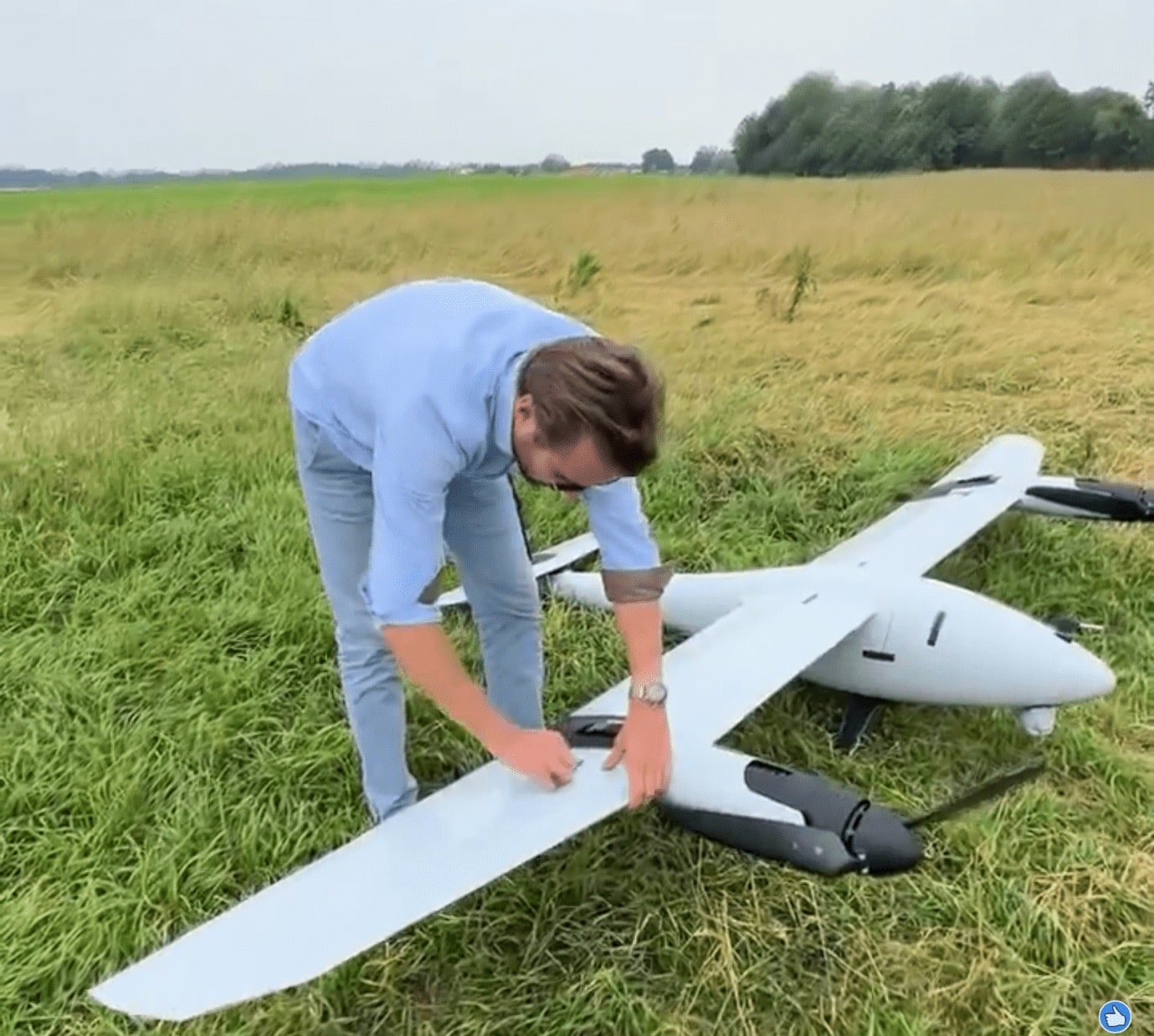 Florian Seibel crouching over a large white fixed-wing VTOL drone in a field.