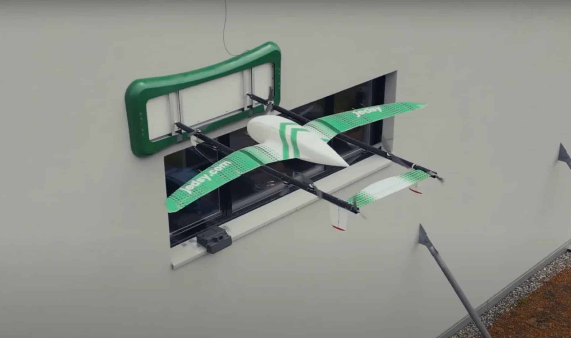 Jedsy delivery drone docked at a green window-mounted landing frame on a wall.