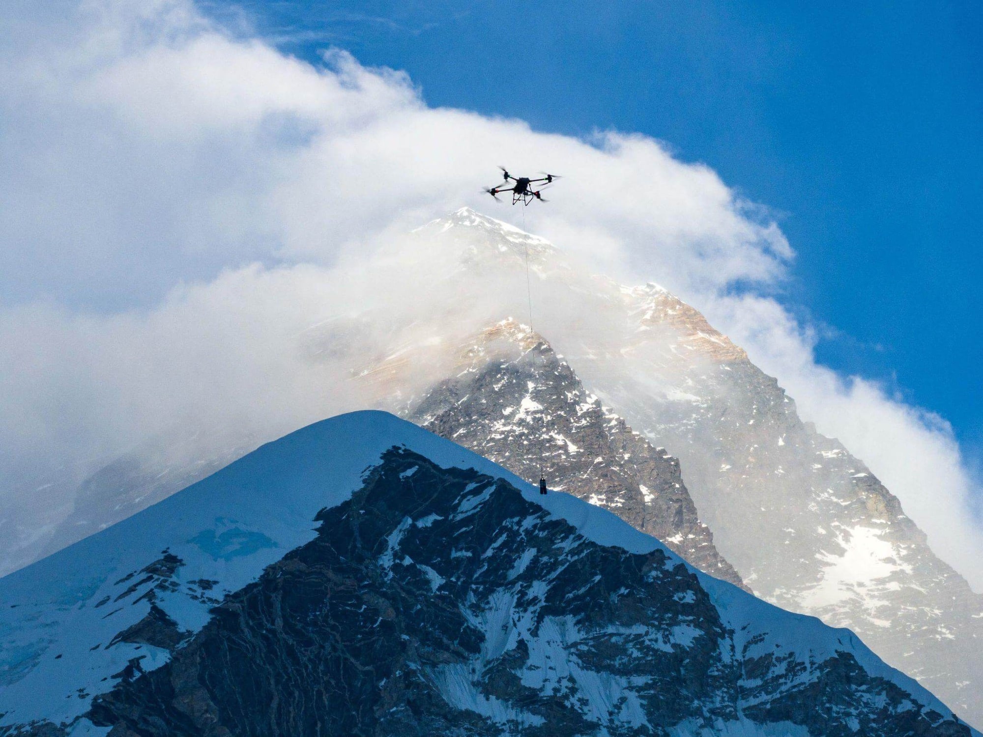 Heavy-lift drone silhouetted against the Everest summit ridge and streaming cloud.