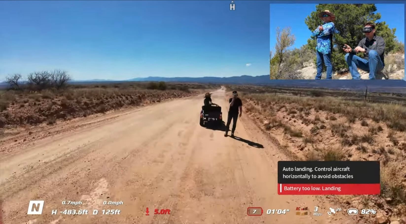 FPV feed of a dirt road with a low battery auto-landing warning on screen.