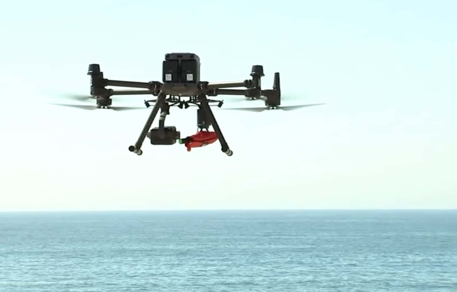 Drone hovering low above the beach with the flotation pack attached below.
