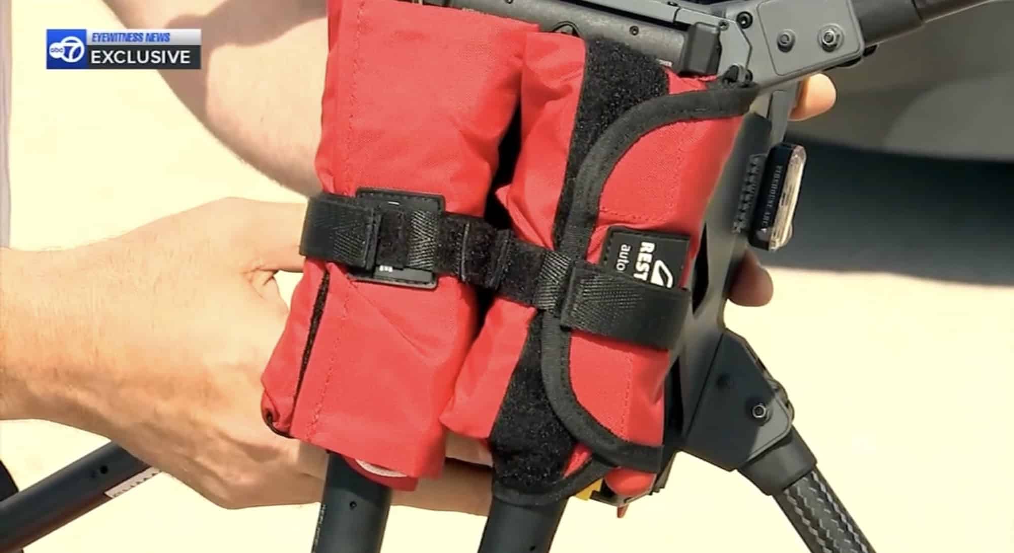 Hands strapping a red Restube flotation pack to the drone landing leg.