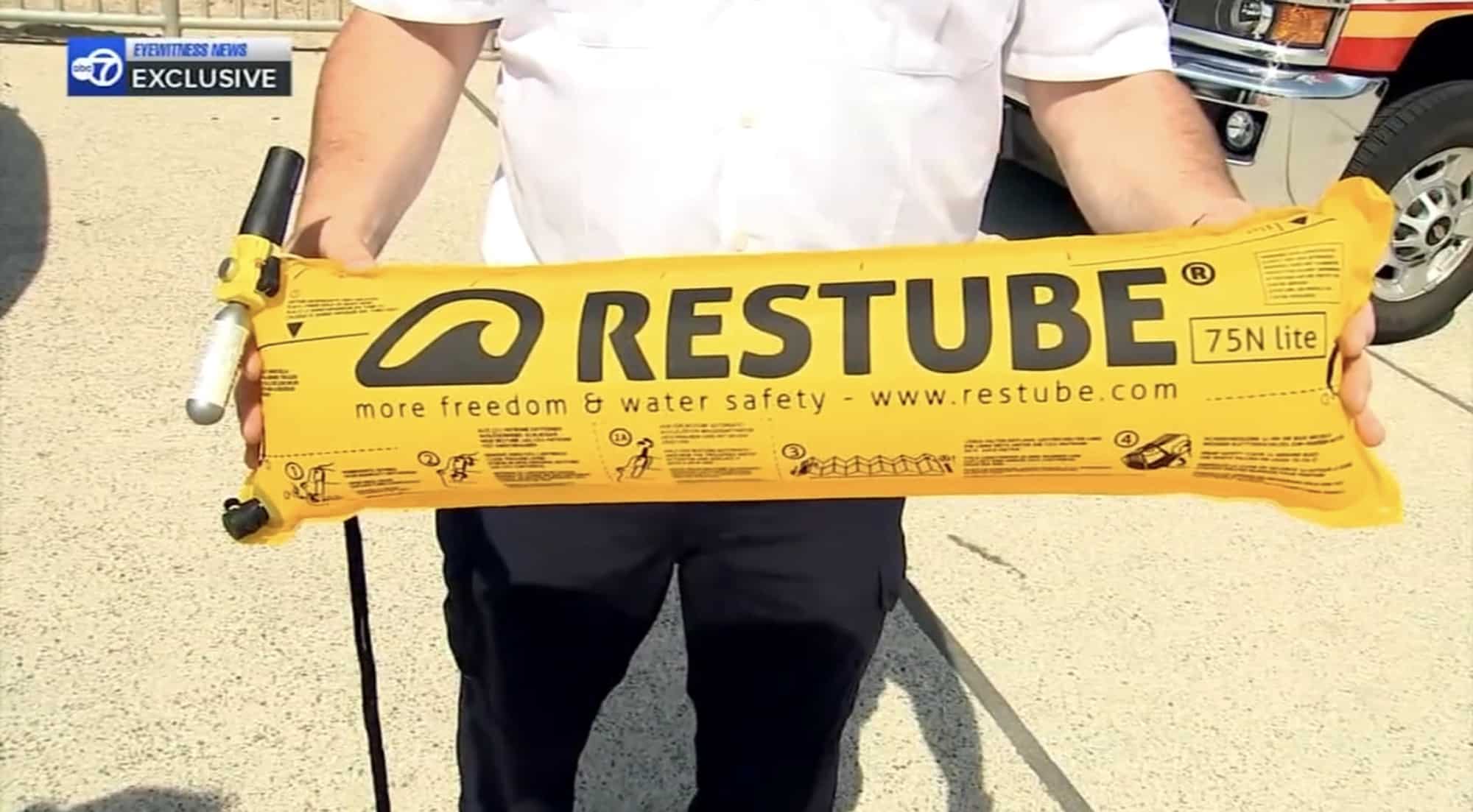 Man holding an unrolled yellow Restube 75N lite flotation tube beside an SUV.