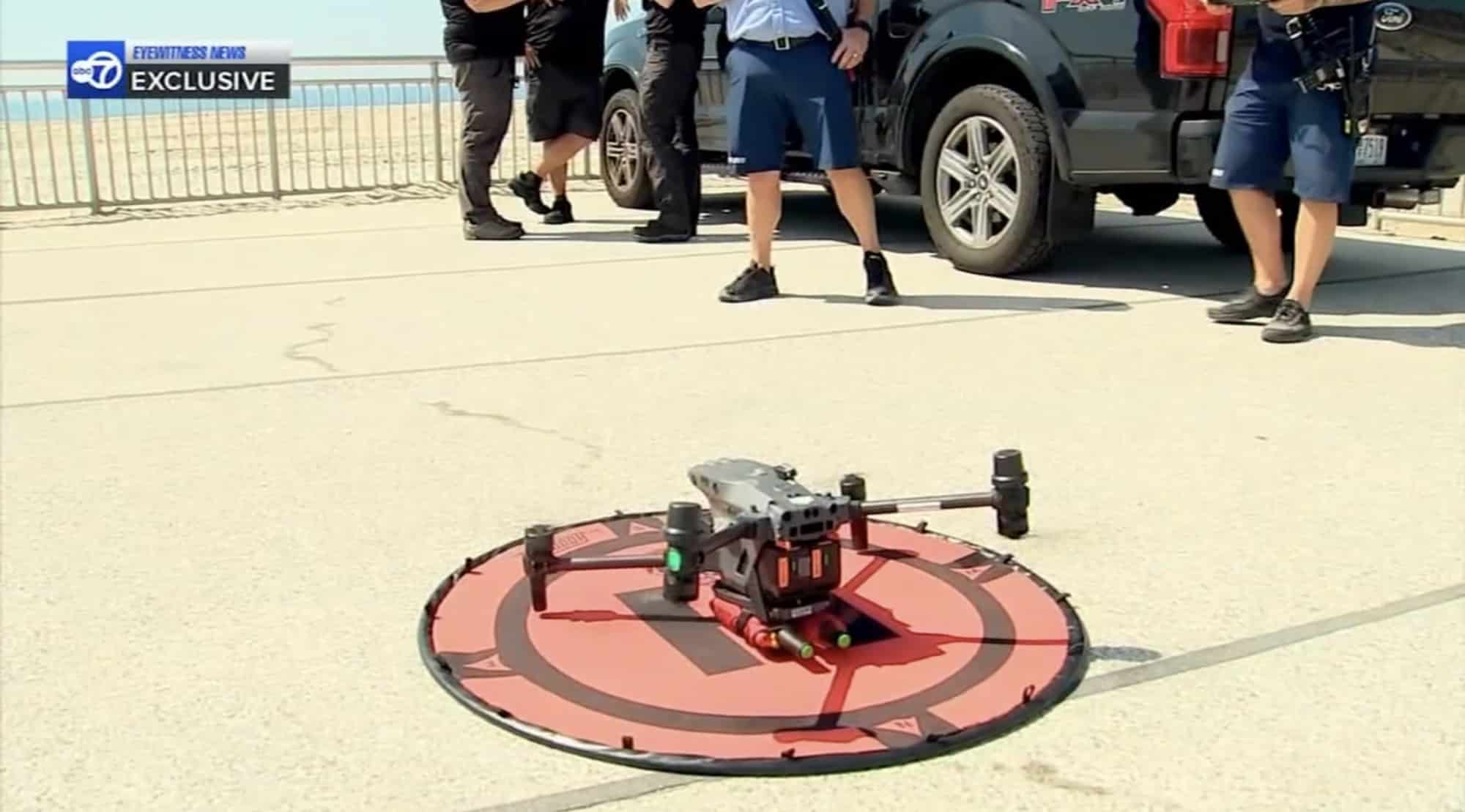 DJI Matrice quadcopter resting on a red landing pad beside a beach parking lot.